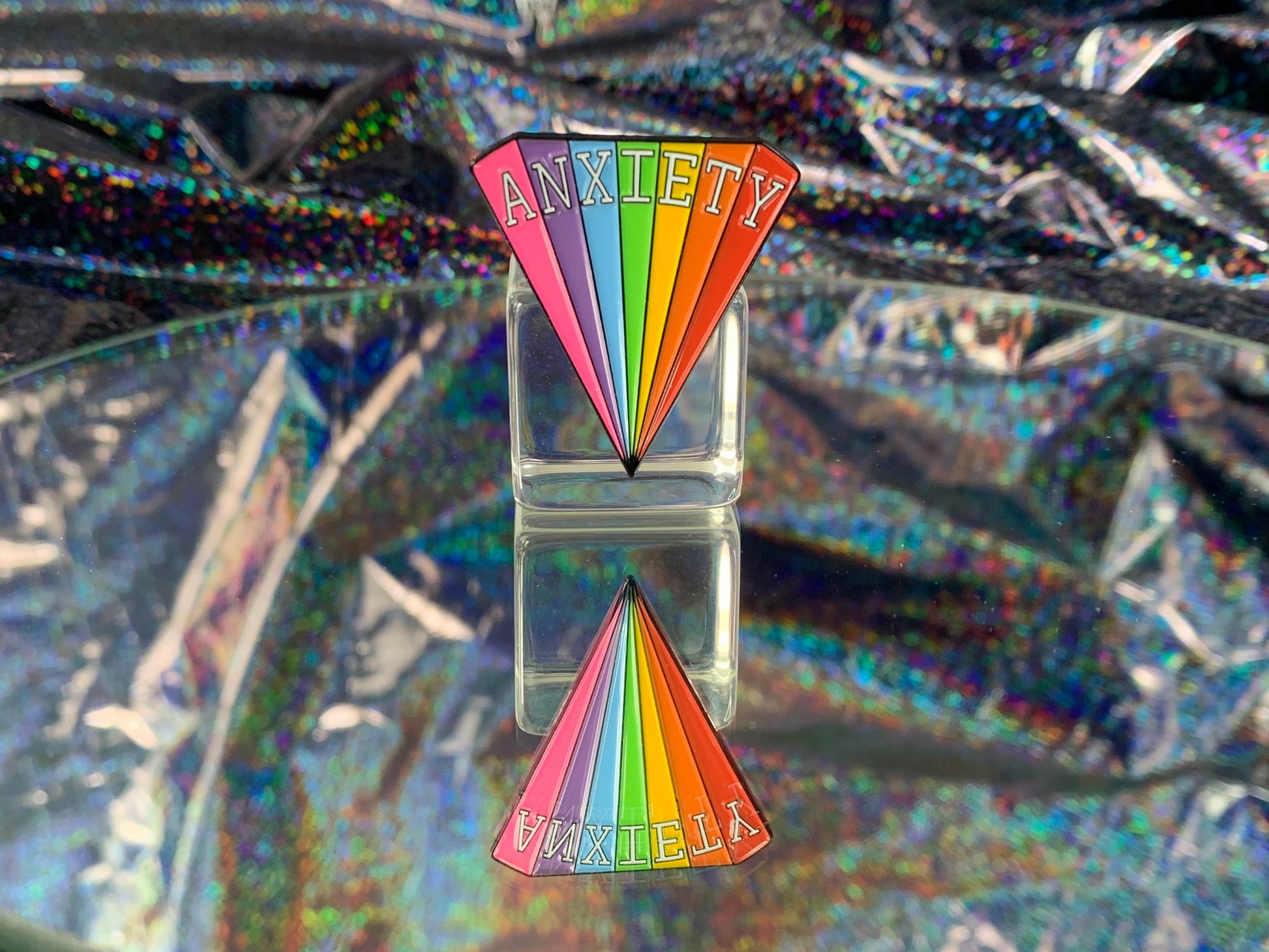 Triangular rainbow enamel pin that reads the word ANXIETY in white text