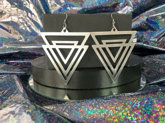 A pair of triangular stainless steel earrings hanging in front of a rainbow glitter background.