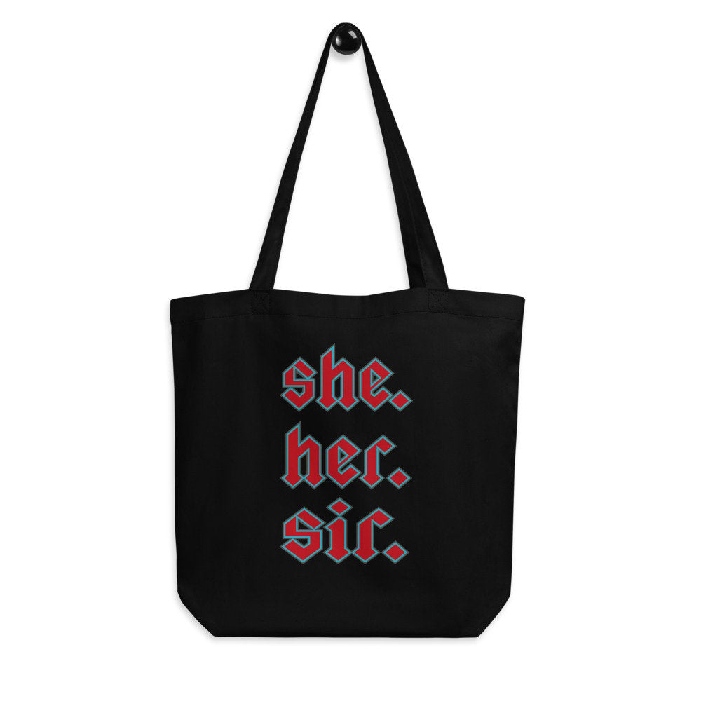 Black tote bag that reads SHE. HER. SIR. in red text with an aqua blue outline, on a white background.