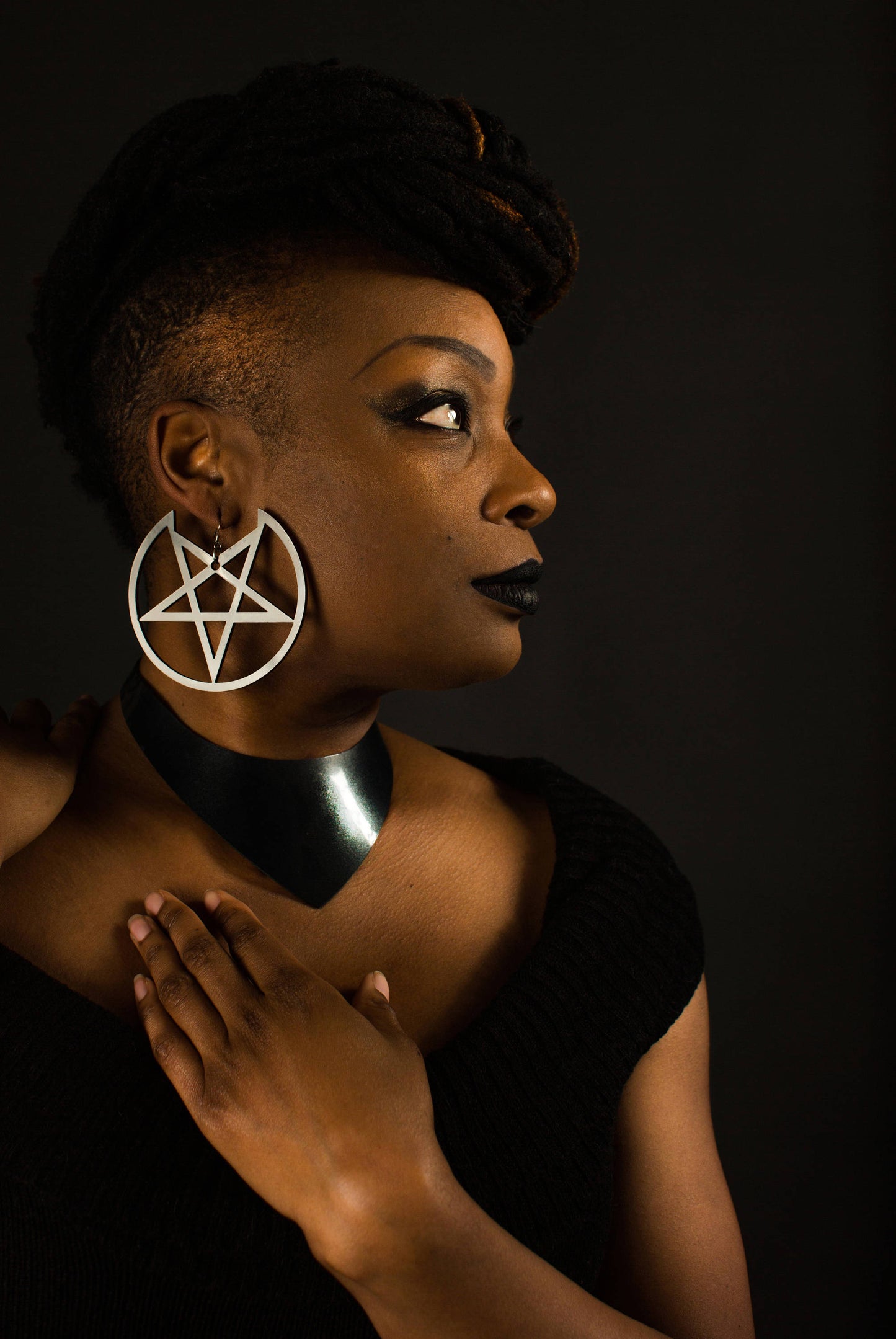 Black femme model looking to the side, wearing large black pentagram shaped earrings laser cut in acrylic.