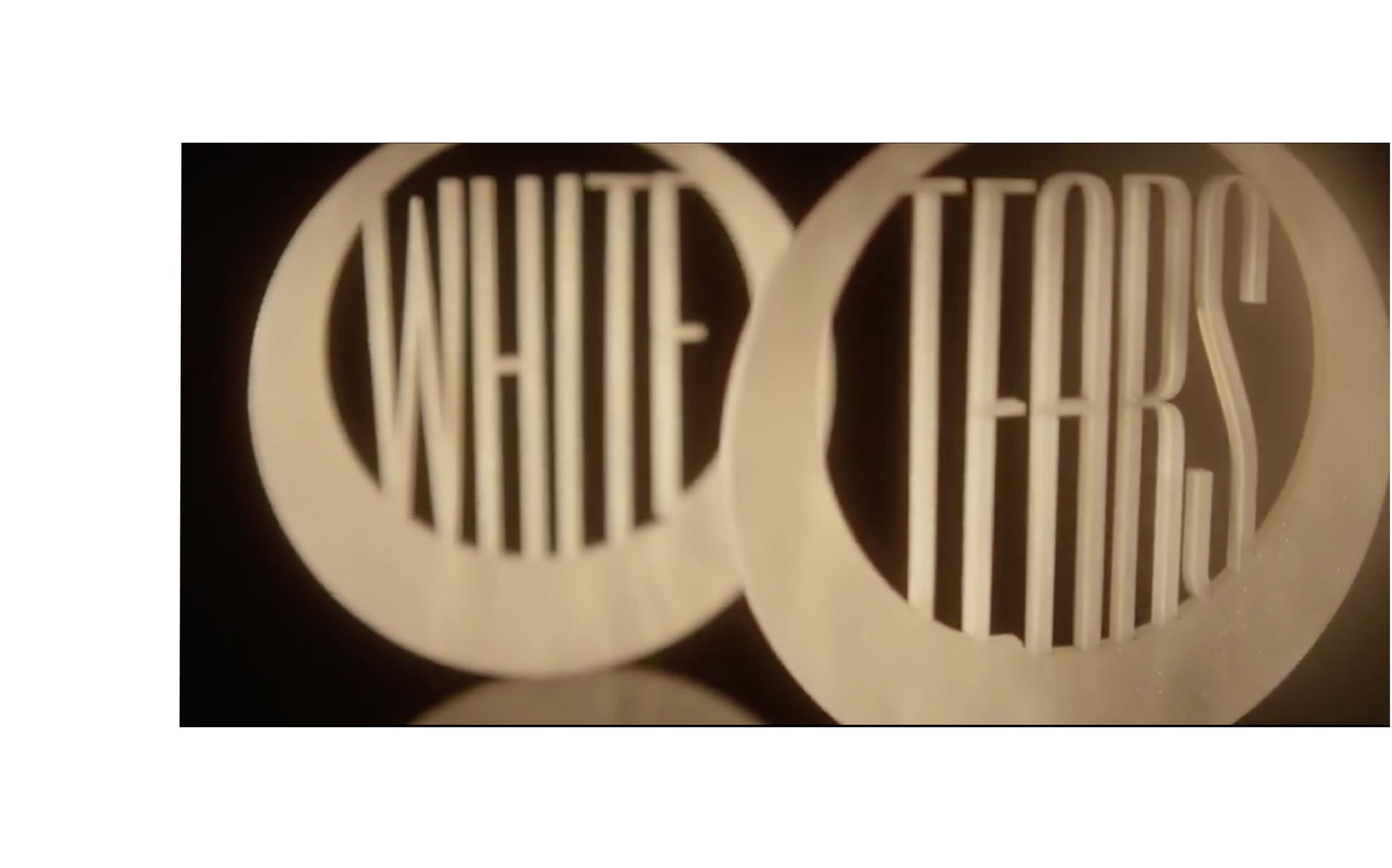White pearlsheen round acrylic earrings, one earring reads the word WHITE and the other reads the word TEARS laser cut into the center of each earring. 