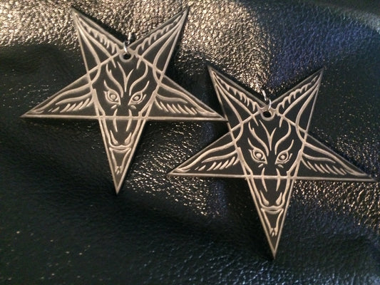 A pair of matte black inverted star-shaped earrings with a Baphomet face laser etched white into the matte black acrylic material.